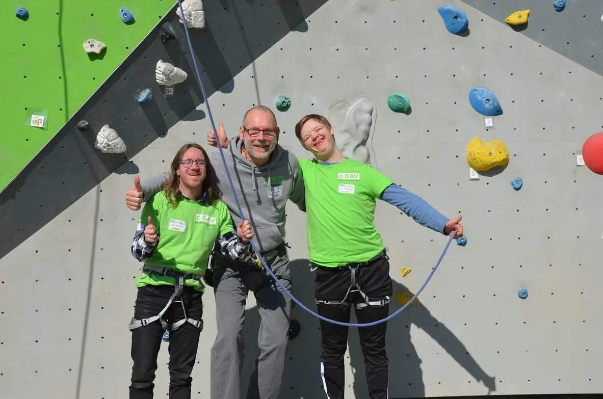 Zwei Kletterer und ein Trainer stehen vor einer Kletterwand und strahlen in die Kamera | © Ralf Holtgrefe
