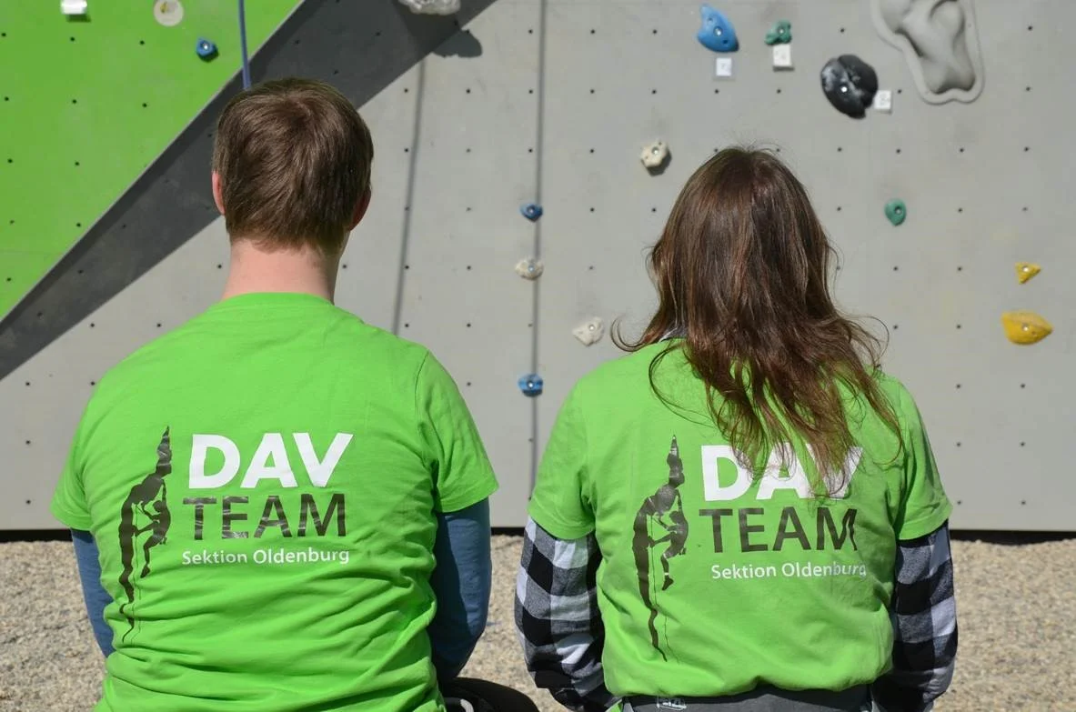 Zwei Kletterer sitzen mit dem Rücken zur Kamera, auf den Shirts steht DAV Team  | © Ralf Holtgrefe