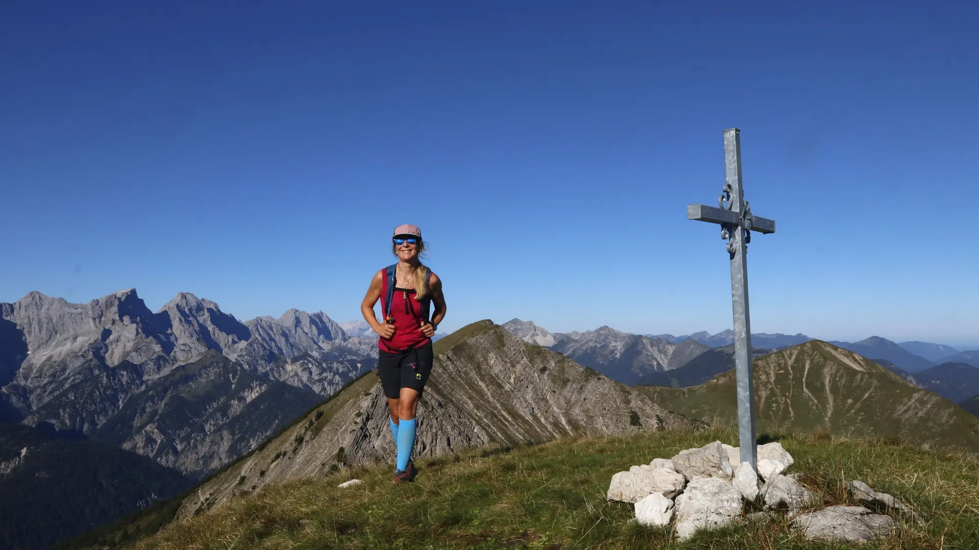 Eine Bergwanderin im Karwendel Gebirge neben einem Gipfelkreuz | © Michael Pröttel