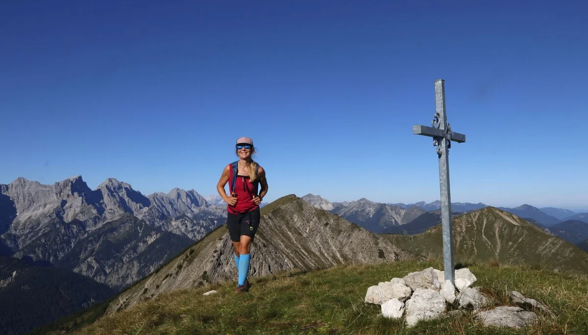 Eine Bergwanderin im Karwendel Gebirge neben einem Gipfelkreuz | © Michael Pröttel