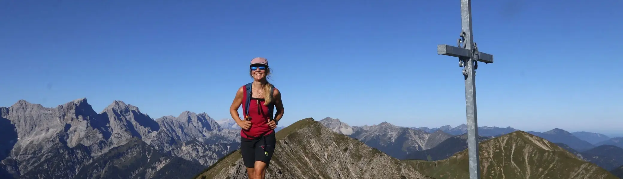 Eine Bergwanderin im Karwendel Gebirge neben einem Gipfelkreuz | © Michael Pröttel
