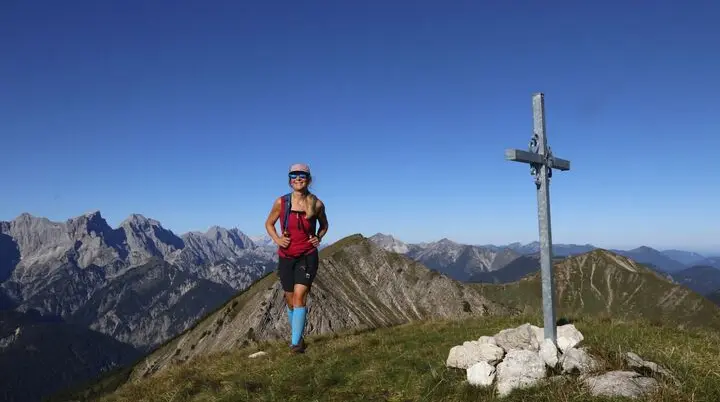 Eine Bergwanderin im Karwendel Gebirge neben einem Gipfelkreuz | © Michael Pröttel