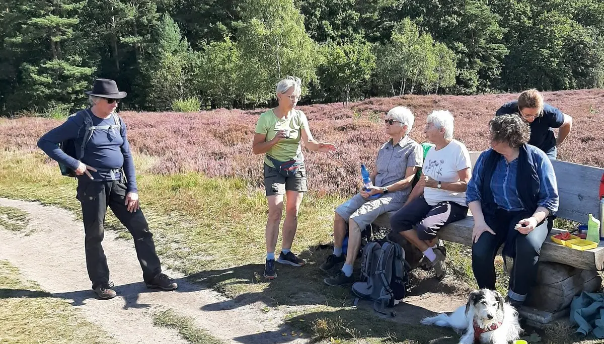 Eine Gruppe Wanderer mit Hund sitzen auf einer Bank, im Hintergrund Heidelandschaft  | © Elke Brüggemann