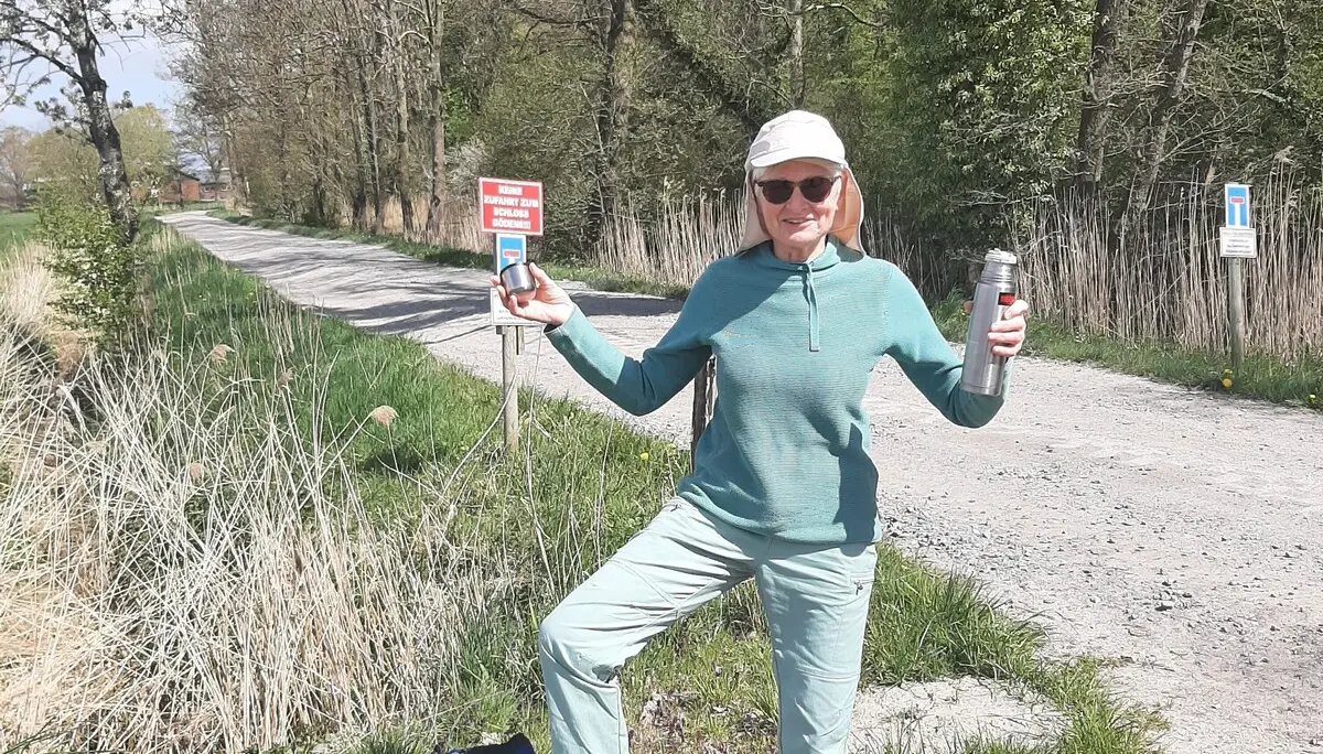 Eine Wanderin steht auf einem Weg, in der Hand hält sie eine Thermosflasche | © Beate Straube